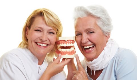 Zahnarzt und Seniorin lachen neben einem Gebissmodell